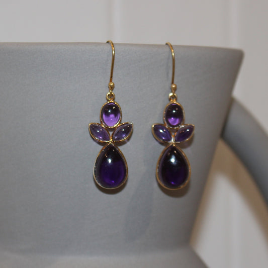 Purple teardrop earrings on a white stand with a white background